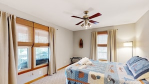 Une chambre à coucher avec un lit, un ventilateur de plafond, une fenêtre donnant sur un beau paysage et une table de chevet.