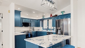 Een moderne keuken met blauwe kastjes, een groot eiland, roestvrijstalen apparatuur en een marmeren aanrecht.