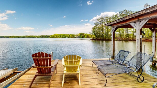 Een houten steiger met twee Adirondack-stoelen en een metalen ligstoel, met uitzicht op een rustig meer.