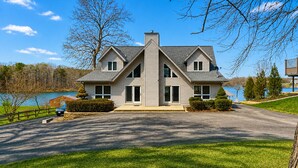 A two-story house with a symmetrical facade, a central chimney, and a driveway leading to a parked car.