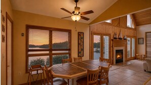 A dining area with a table and chairs, a fireplace, and large windows with a view of the outdoors.