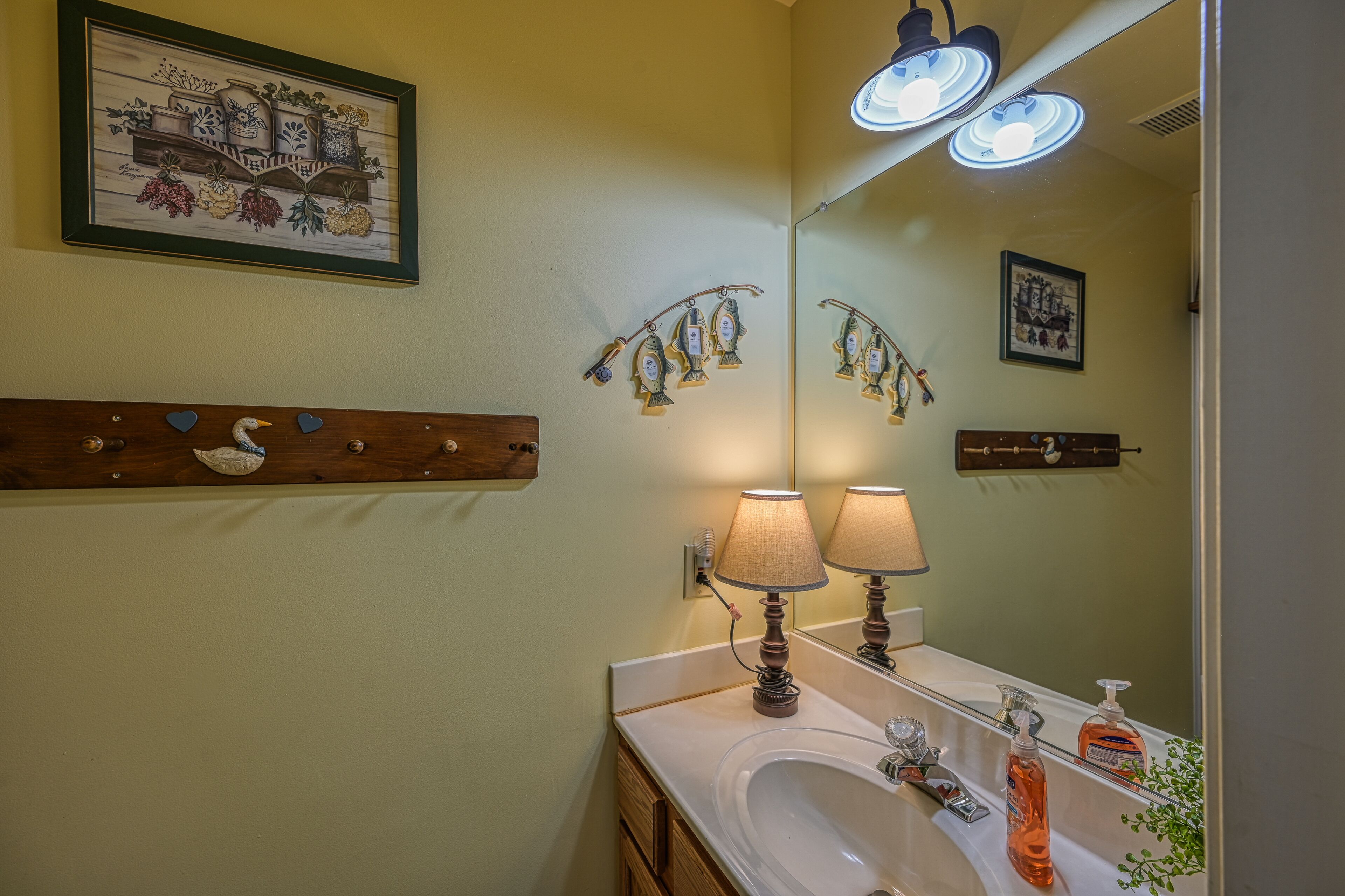 A bathroom with a sink, two lamps, a mirror, and decorative items.