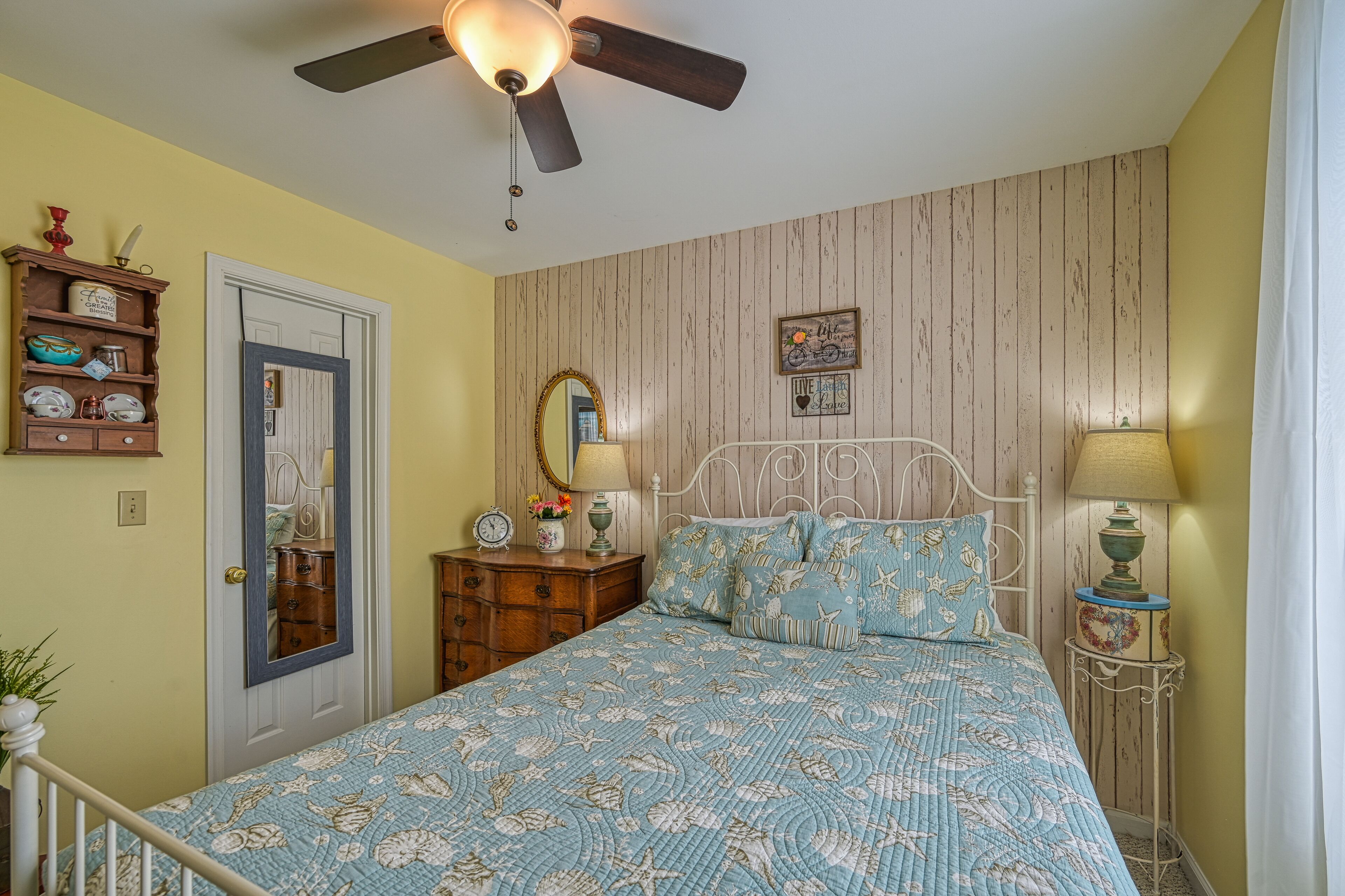 A bedroom with a bed, a dresser, a mirror, and a ceiling fan.