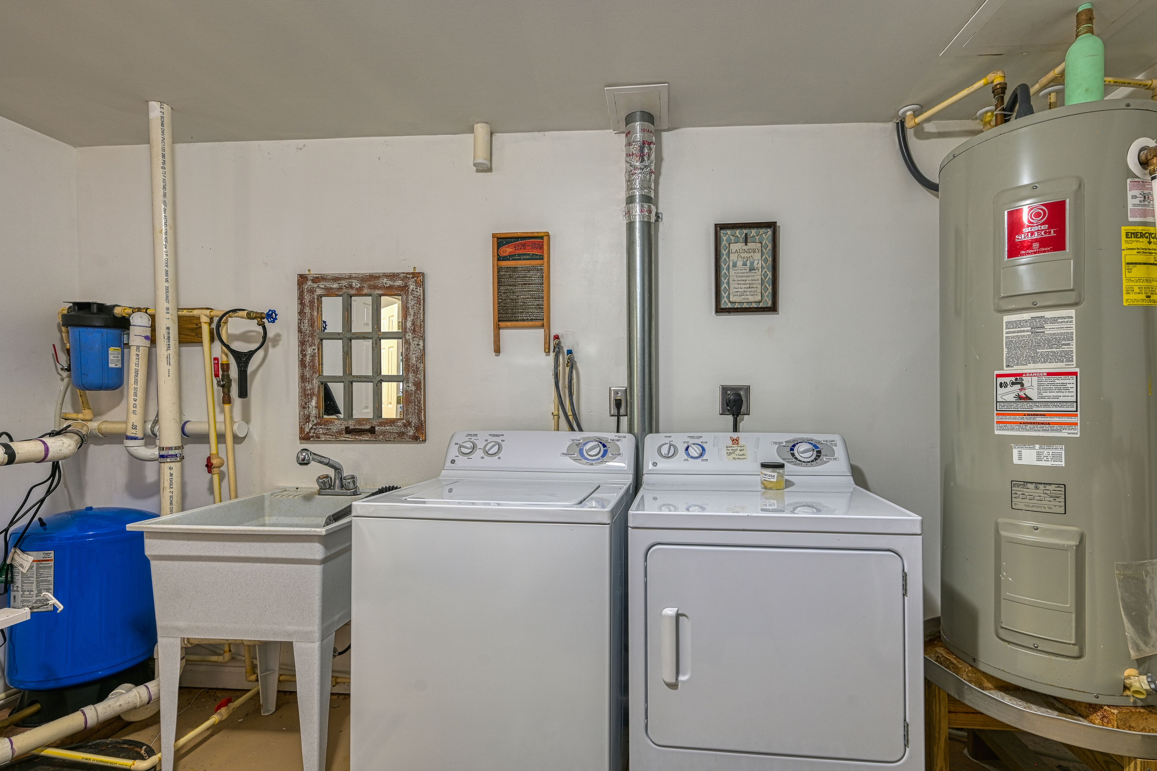 A laundry room with two washing machines, a large water heater, and various pipes and hoses.