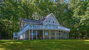 A large, two-story house with a wrap-around porch and a staircase leading to the upper level. - Stunning lakeside home with dock, large deck, kayaks, firepit, & pool table (Bumpass)