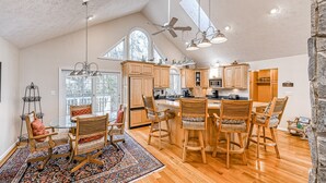 A spacious kitchen with wooden cabinets, a central island, and a dining area with bar stools. - Stunning lakeside home with dock, large deck, kayaks, firepit, & pool table (Bumpass)