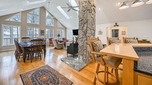 A spacious living area with a stone pillar, wooden furniture, and large windows. - Stunning lakeside home with dock, large deck, kayaks, firepit, & pool table (Bumpass)