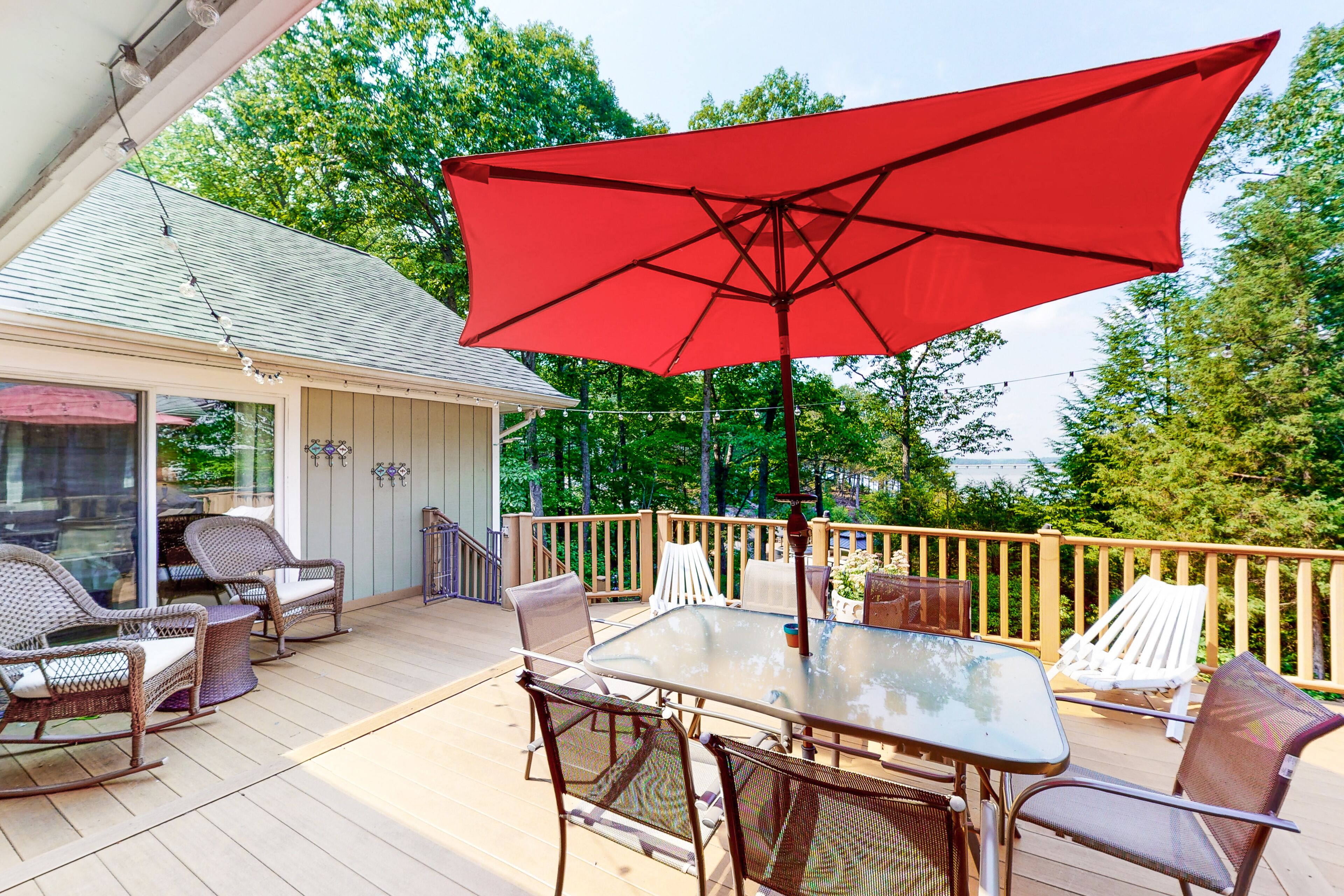 A covered patio with wicker furniture, a glass table, and a red umbrella.