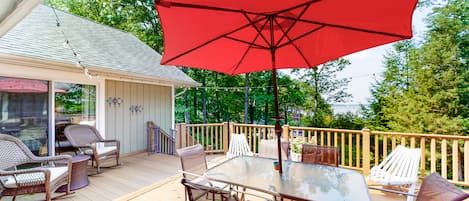 A covered patio with wicker furniture, a glass table, and a red umbrella.