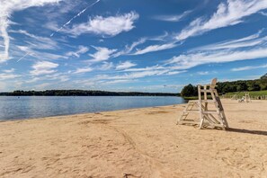 A beach with a lifeguard tower and a calm lake under a clear sky.
