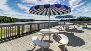 Una terraza con mesas de picnic y sombrillas a rayas azules y blancas, con vista a una masa de agua.