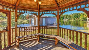 Un belvédère en bois avec un banc, d’où l’on a vue sur un lac et une maison.