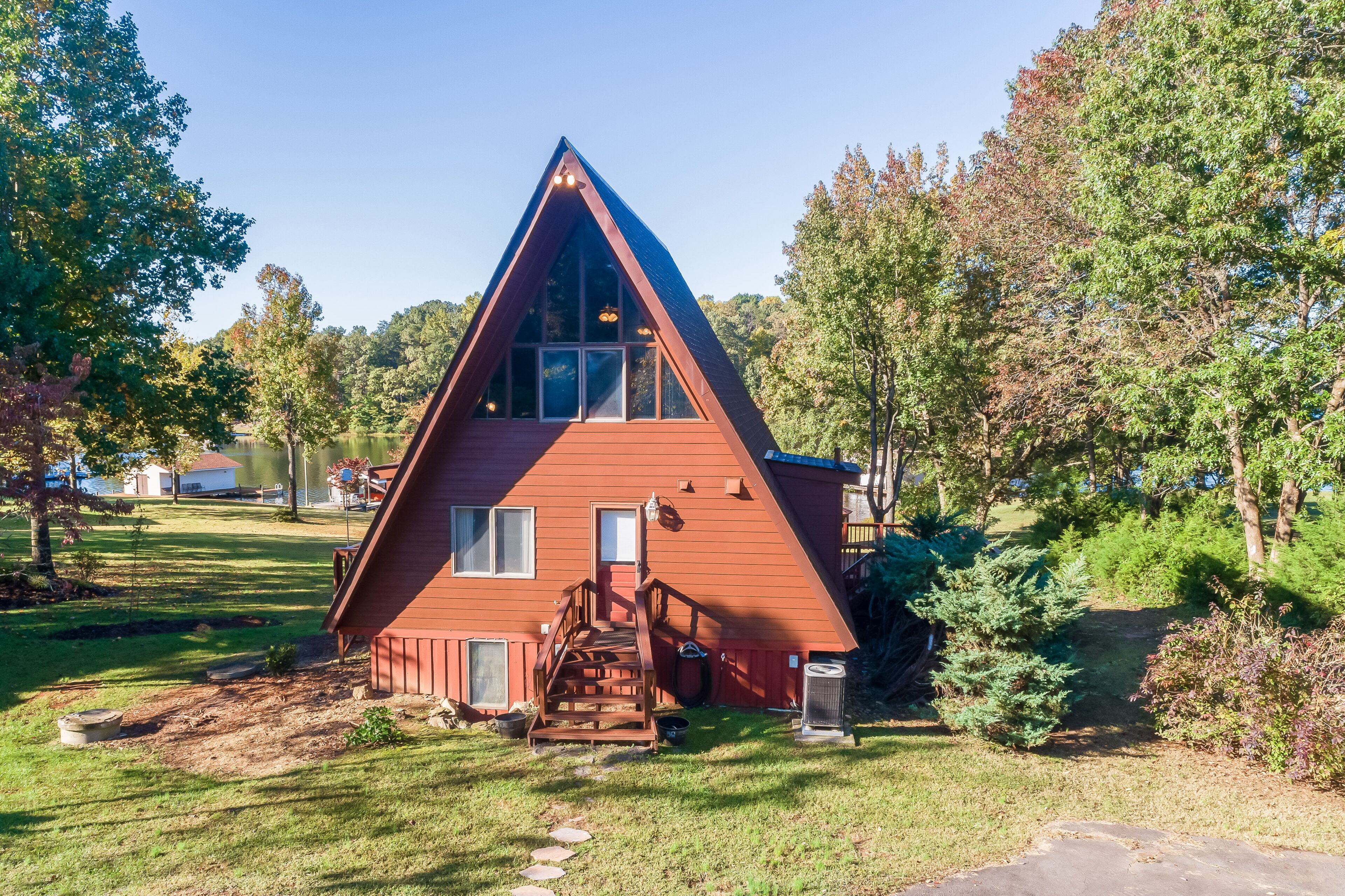 Una casa roja de forma triangular con una escalera de madera que conduce a la entrada, rodeada de árboles y un jardín cubierto de césped.