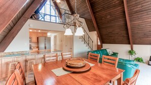 Un grand espace à manger avec une table et des chaises en bois, une cuisine à l’arrière-plan et un escalier menant à l’étage supérieur.