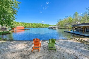 Näkymä järvelle, jossa on kaksi Adirondack-tyylistä tuolia järvelle päin, laituri ja pieni mökki.