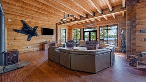 A spacious living room with a large sectional sofa, wooden ceiling beams, and a stone fireplace. - Lakefront Cabin w/ Hot Tub, Boat Dock, WiFi, a Game Room & Firepit - Dogs OK (Mineral)