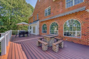 A wooden deck with a stone table and benches, surrounded by a brick house with large arched windows.