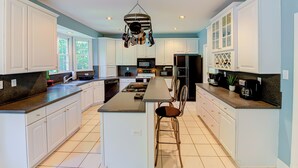 Una cocina amplia con gabinetes blancos, una isla central y un colgador para ollas.