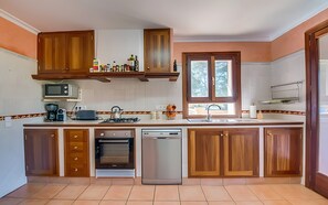 A kitchen with wooden cabinets, a microwave, a toaster, a kettle, a sink, and a dishwasher. - Villa 'Son Grau' with Mountain Views, Private Pool, and Wi-Fi (Alaró)