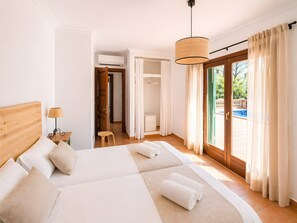 A hotel room with a large bed, a small table with a lamp, a chair, and a view of a pool through the glass door. - Villa 'Son Grau' with Mountain Views, Private Pool, and Wi-Fi (Alaró)