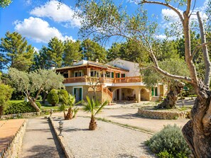 A two-story house with a balcony, surrounded by trees and a gravel path. - Villa 'Son Grau' with Mountain Views, Private Pool, and Wi-Fi (Alaró)