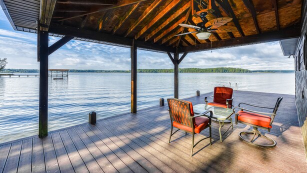 Un patio in legno coperto con tavolo e sedie, affacciato su un lago tranquillo.