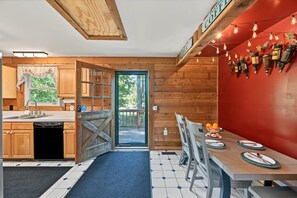 A kitchen with wooden cabinets, a dining area with a table set for two, and a red accent wall. - Lakefront Dog Friendly with boat mooring, deck, hot tub, game room & fast WiFi (Bumpass)