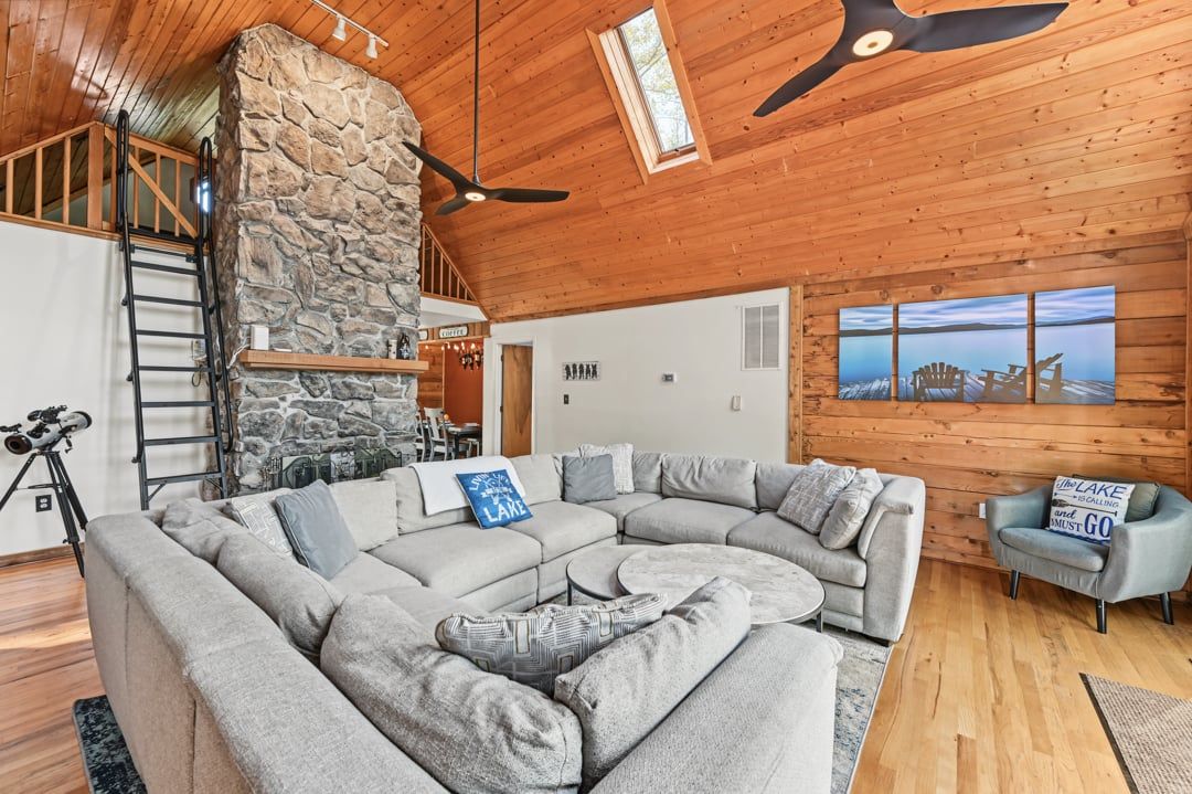 A cozy living room with a stone fireplace, a large sectional sofa, and a ceiling fan.