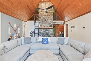 Ein modernes Wohnzimmer mit Kamin aus Stein, einem großen L-förmigen Sofa und einem Deckenventilator.