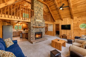 Eine geräumige Lodge mit Kamin aus Stein, Holzbalkendecke, Küche und Wohnbereich mit Sofas und Fernseher.