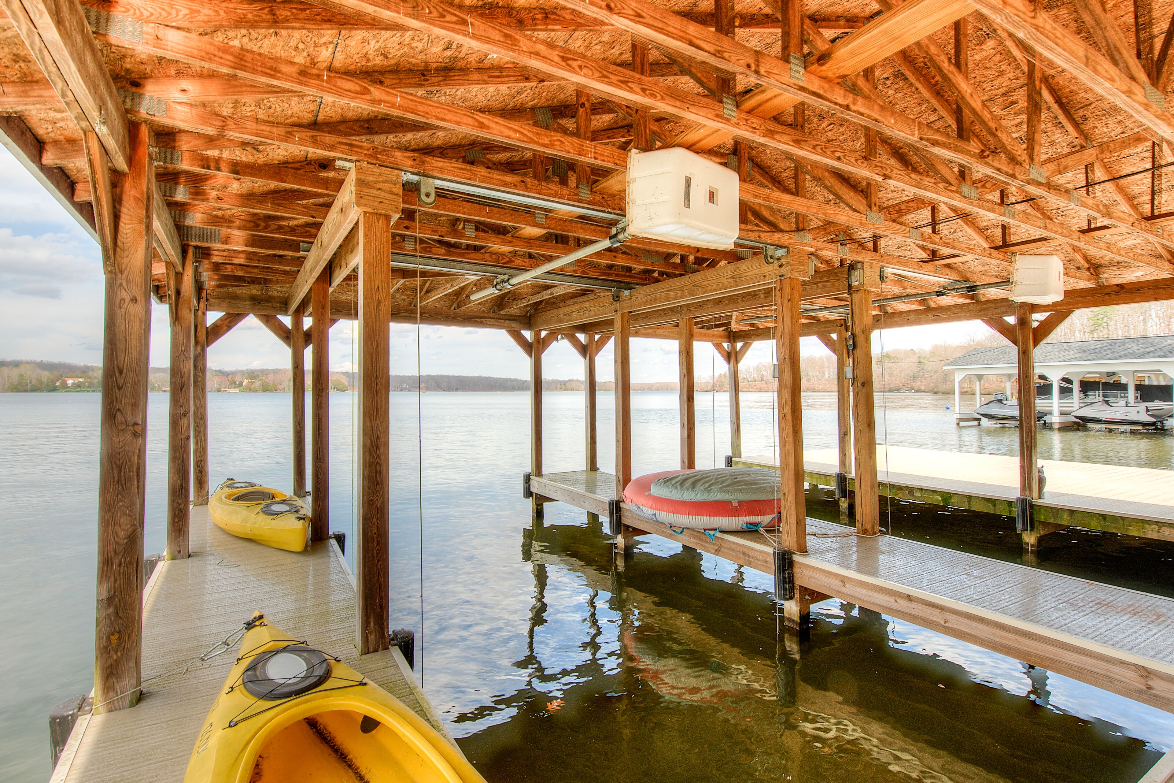 A wooden dock extending into a calm lake, with kayaks and a paddleboard docked at the end.