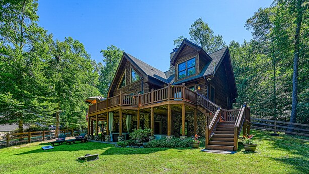A large wooden house with a covered porch, a staircase, and a fenced yard.