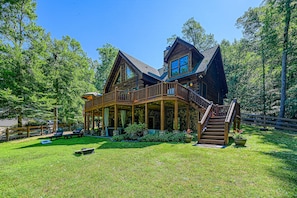 A large wooden house with a covered porch, a staircase, and a fenced yard.
