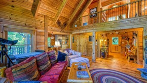 A spacious log cabin interior with a large living area, a balcony, and a cozy fireplace.