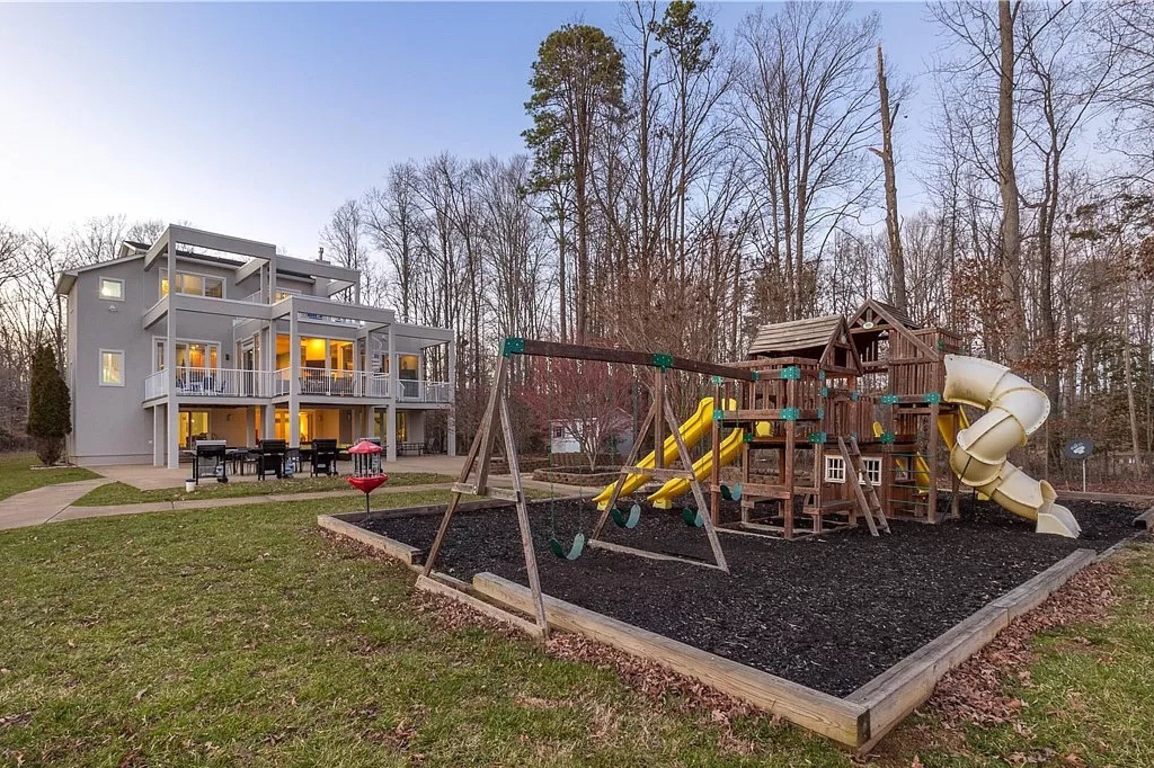A modern two-story house with a balcony, a playground with slides, and a well-maintained lawn.