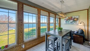 Keittiössä on suuret ikkunat, ruokapöytä, baarituolit, sohva ja lamppu.