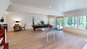 A spacious room with a pool table, a ping pong table, and a billiards table. There are large windows providing natural light and a view of the outdoors. - Pet Friendly, pool table, ping pong, fire pit, free WIFI (Bumpass)