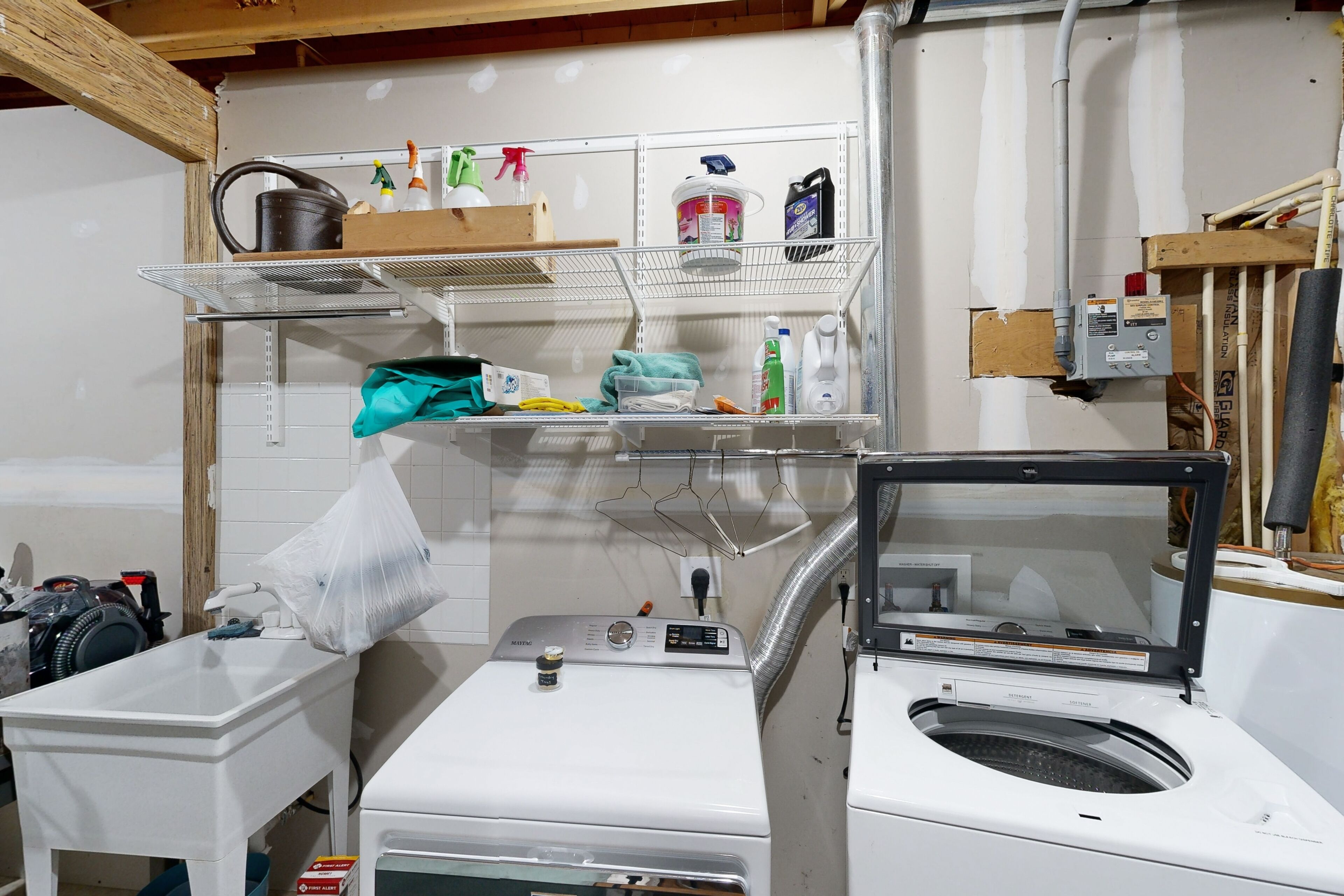 Una sala de bugaderia amb rentadora, assecadora i prestatgeries amb productes de neteja.