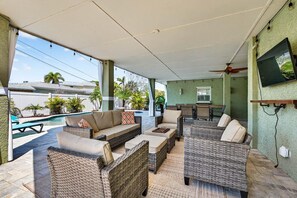 An outdoor patio with wicker furniture, a pool, and a television mounted on the wall. - Blue Lagoon 3BR Pool Home Near the Beach (Redington Beach)
