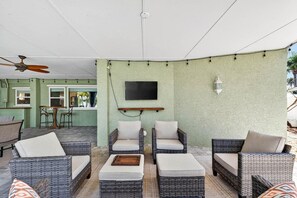A covered outdoor seating area with wicker furniture, a ceiling fan, and a mounted TV. - Blue Lagoon 3BR Pool Home Near the Beach (Redington Beach)