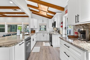 A modern kitchen with white cabinetry, a marble countertop, and a wooden ceiling beam structure. - Blue Lagoon 3BR Pool Home Near the Beach (Redington Beach)