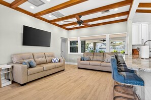 A spacious living area with a large flat-screen TV, two sofas, a coffee table, and a bar area with stools. - Blue Lagoon 3BR Pool Home Near the Beach (Redington Beach)
