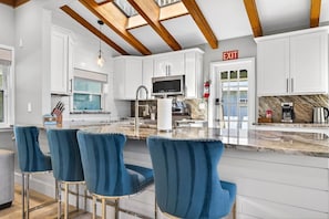 A modern kitchen with white cabinets, a marble countertop, and blue bar stools. - Blue Lagoon 3BR Pool Home Near the Beach (Redington Beach)