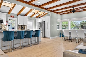 A modern kitchen with a bar area, wooden ceiling beams, and a dining space with white chairs. - Blue Lagoon 3BR Pool Home Near the Beach (Redington Beach)