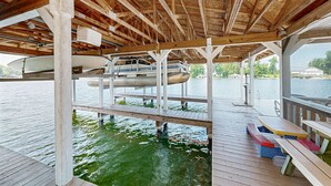 Una terraza de madera con un barco amarrado debajo, una zona de estar cubierta con bancos y vistas al agua.