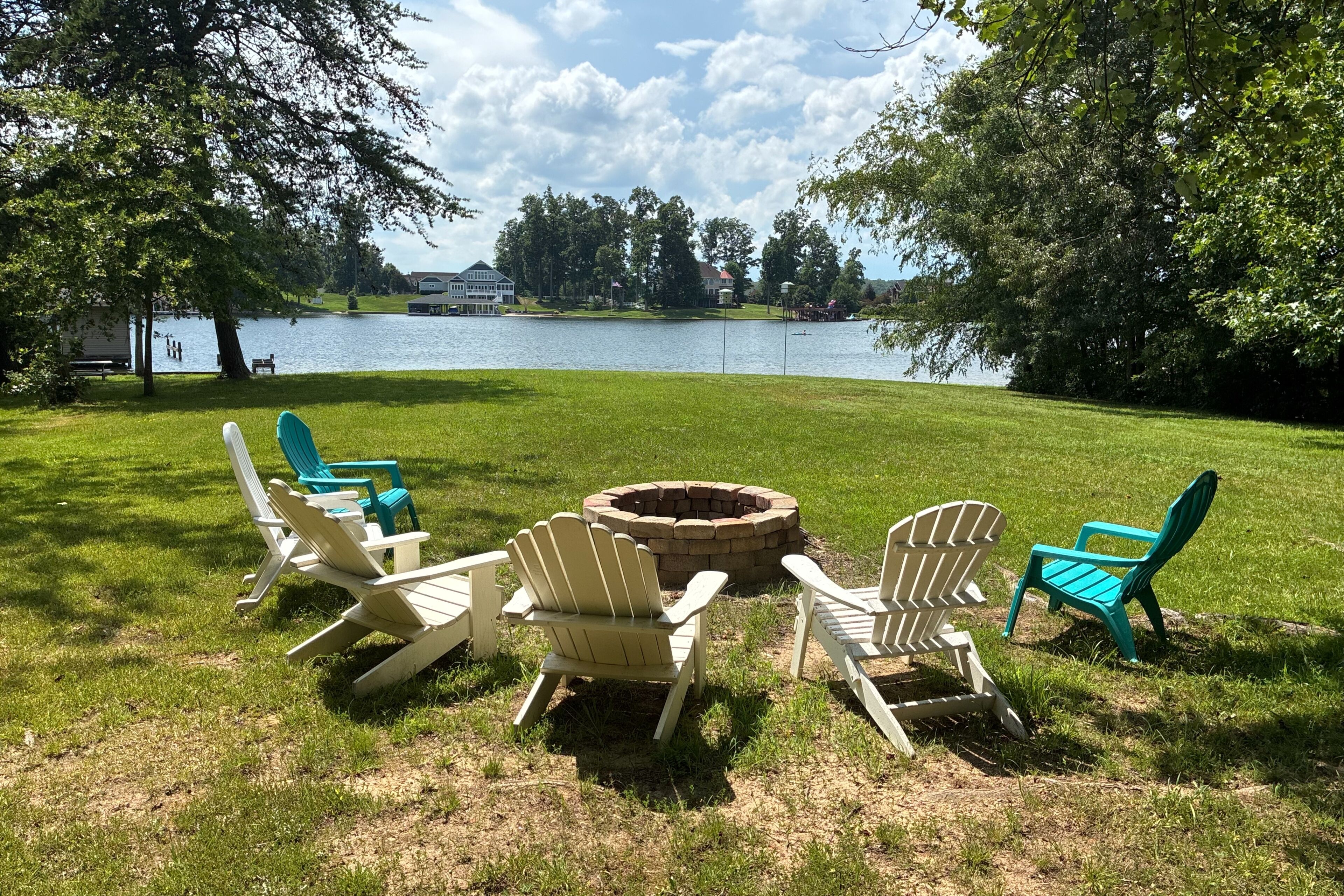 A lakeside outdoor seating area with Adirondack chairs and a fire pit.