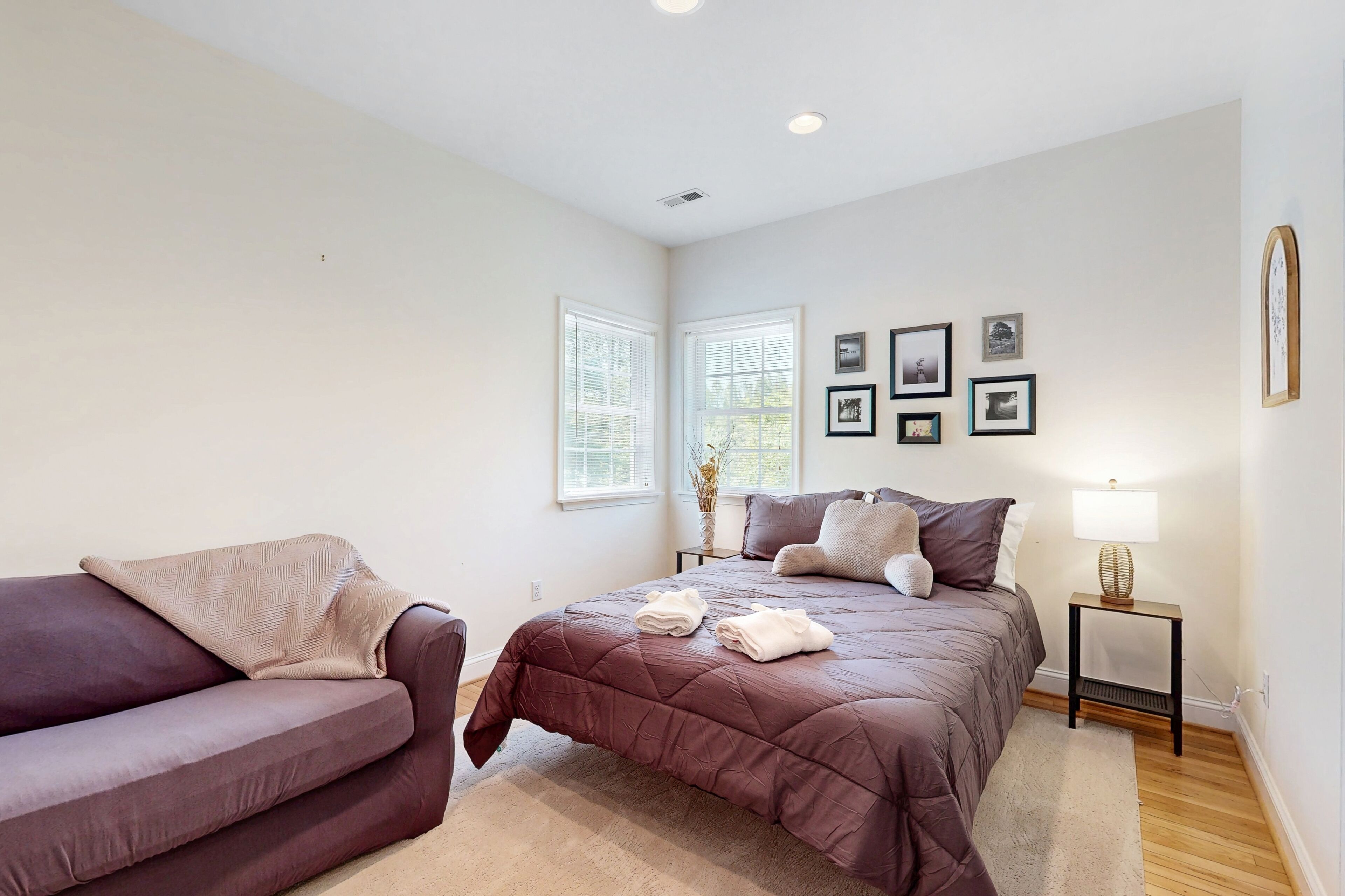 A bedroom with a bed, a sofa, a nightstand, and framed pictures on the wall.