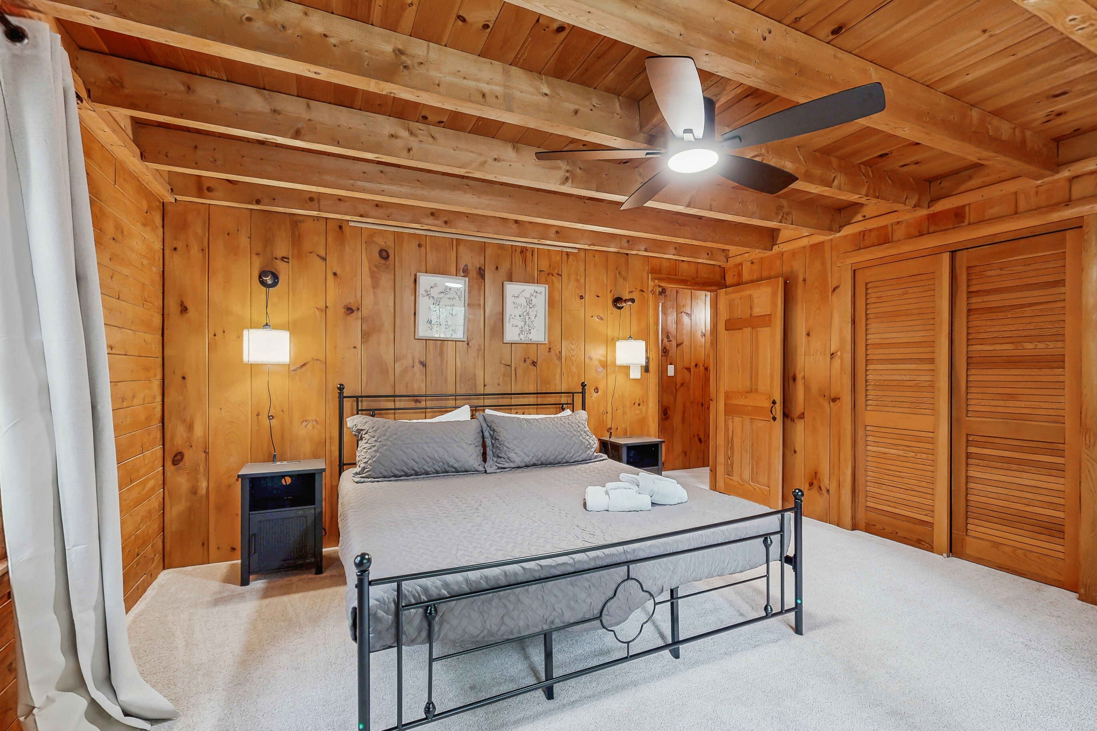 Une chambre à coucher aux murs lambrissés, avec un lit, des lampes de chevet, un ventilateur de plafond et une armoire.