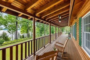 A covered wooden deck with a railing, wooden benches, and a view of a lake and trees.