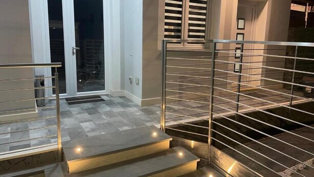 Una escalera moderna con barandillas de metal y peldaños iluminados que conducen a una puerta con paneles de vidrio.